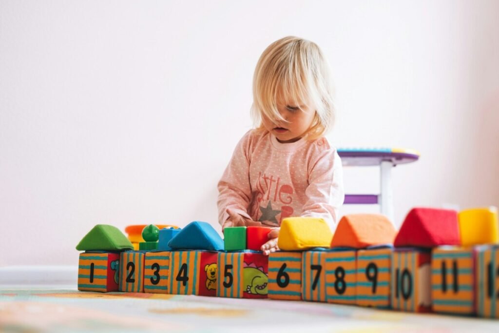 Little girl toddler in pink playing with blocks with numbers in children's room at home