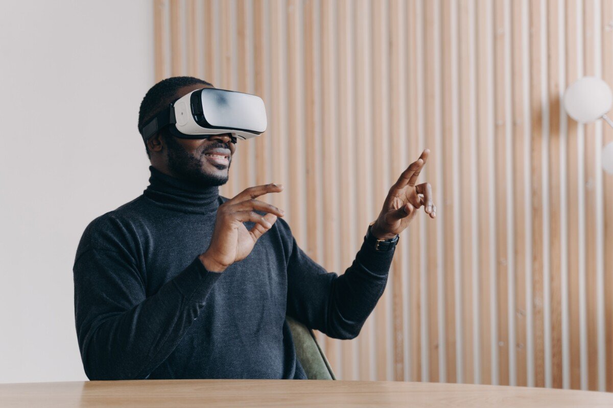 Young joyful African man office worker in VR headset glasses playing favorite 3D game